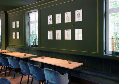 Stilvolle Innenansicht von Lilliys Parkcafe in Bückeburg mit grün gestrichenen Wänden, Polsterbänken, Holz­tischen und Wandbildern.