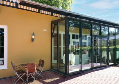 Glasvorbau von Lillys Parkcafe in Bückeburg mit Außensitzplatz und gelber Fassade nach der Renovierung.