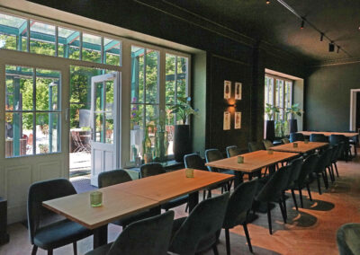 Innenraum von Lillys Parkcafe mit Blick durch große Fenster und offene Türen auf die sonnige Terrasse im Schlosspark Bückeburg.